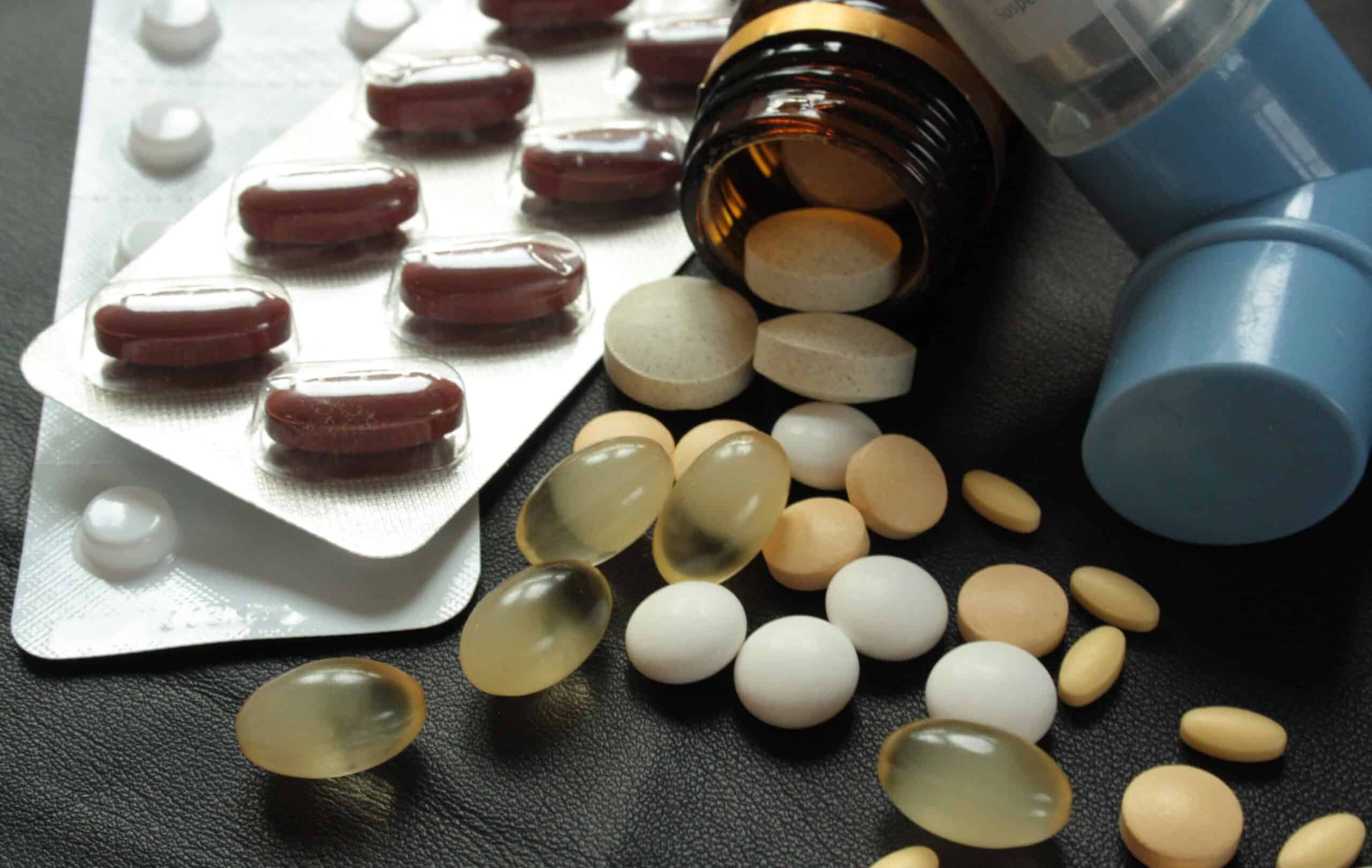 Verschiedenfarbige Tabletten, Kapseln und ein Dosieraerosol auf dunklem Untergrund